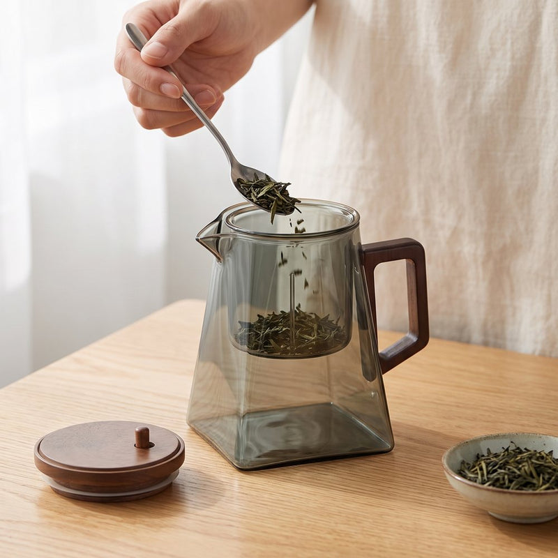 Une main dépose des feuilles de thé dans la coupelle en verre